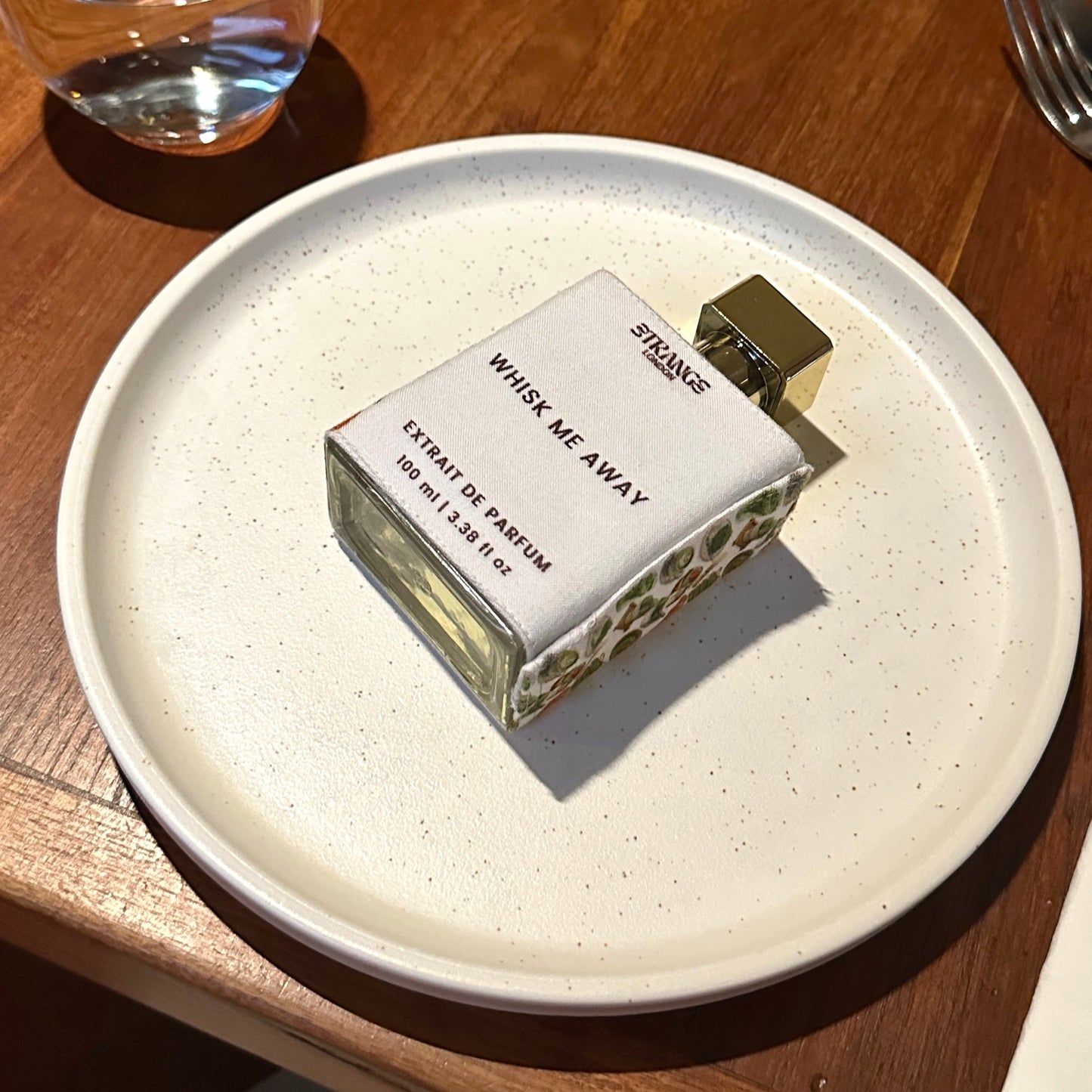 Perfume bottle on a white plate with a glass of water in the background