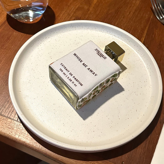 Perfume bottle on a white plate with a glass of water in the background