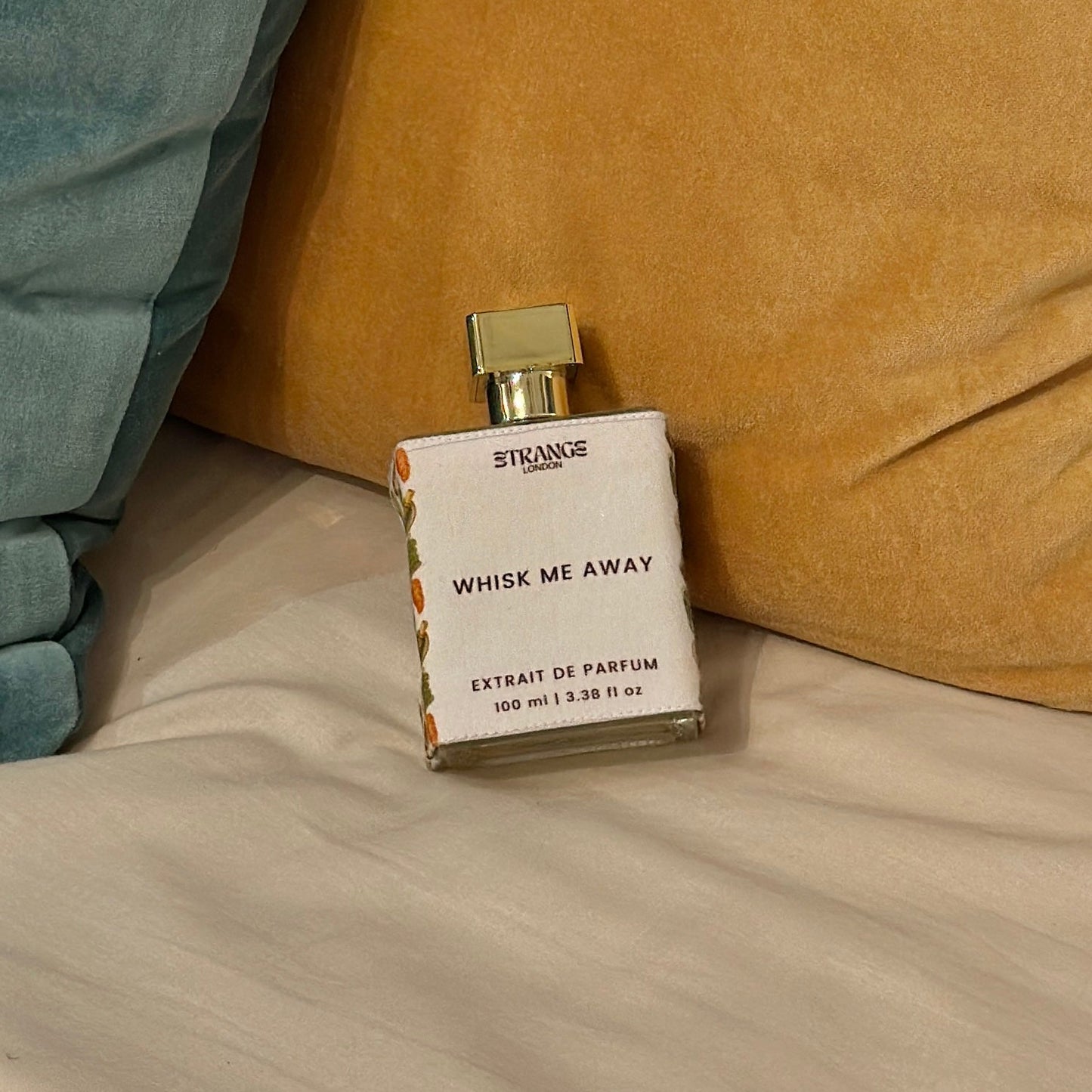 Perfume bottle labeled 'Whisk Me Away' on a bed with pillows.